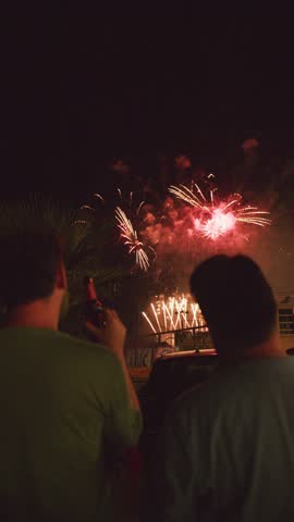 Two people enjoy a stunning fireworks display illuminating the night sky, bursting with colors and patterns. The atmosphere is festive and lively, perfect for celebrating special moments.