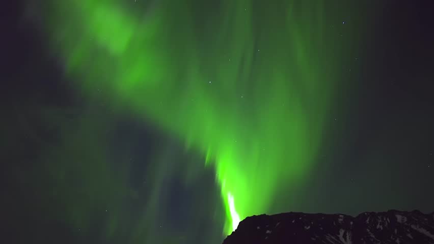 Bright green northern lights sweeping across the sky above snowy mountains in the Arctic Circle, filmed in pristine 4K quality under a star-filled sky.