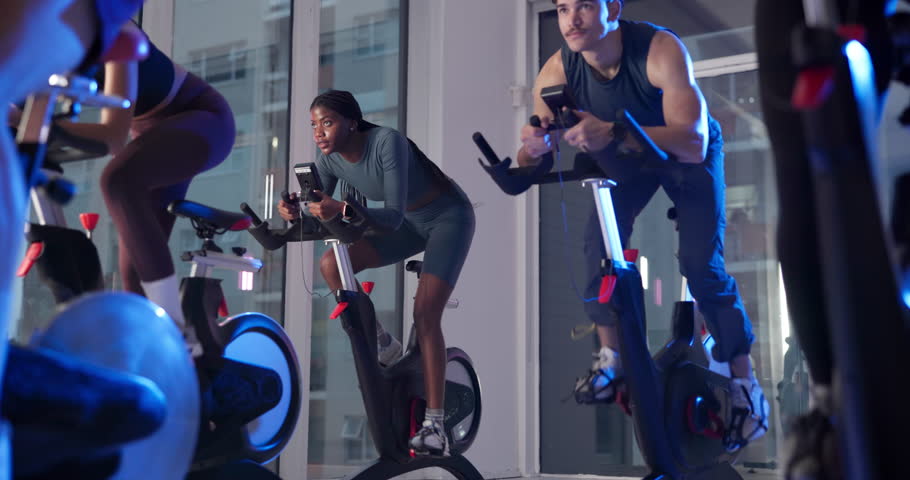 Bike, fitness and group with people in spin class for cardio improvement or cycling at night. Exercise, training performance and stationary spinning with athletes in gym for late evening challenge