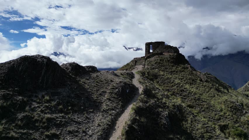 Aerial view of majestic Inti Punku Hike with ancient ruins, rugged mountains, and expansive valley under dramatic clouds, Ollantaytambo, Cusco, Peru.