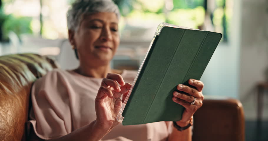 Senior woman, hands and tablet on sofa for playing online bingo, gambling app or internet surfing. Retirement, person or relax with digital tech in home for gaming site, streaming service or research