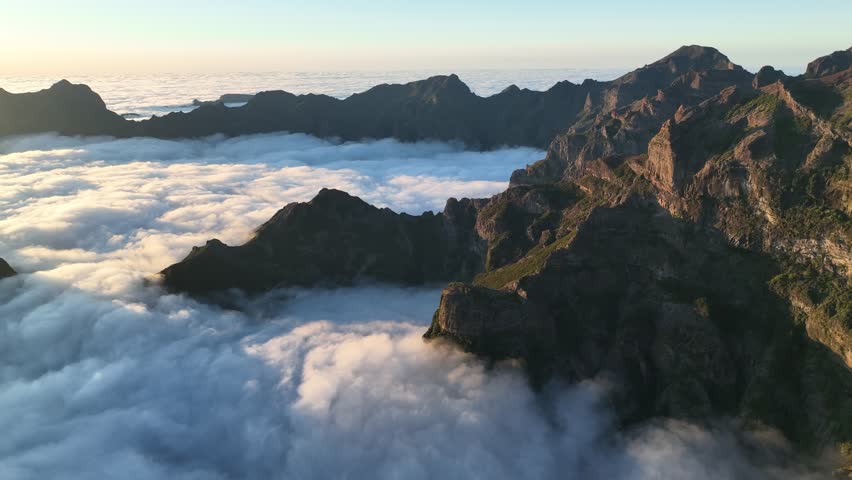 Aerial view of rugged pico do arreiro surrounded by majestic mountains and clouds at sunrise, Curral das Freiras, Madera, Portugal.
