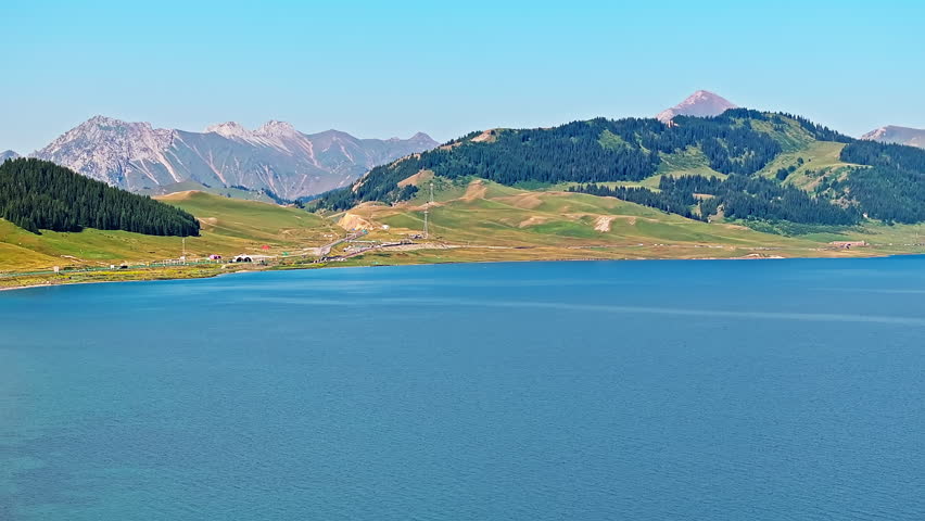 Aerial shot of the beautiful Sayram Lake natural landscape in Xinjiang. Blue lake and green forest with mountain range scenery in China.