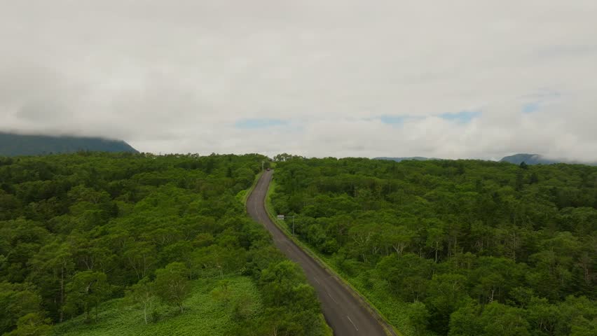 Aerial tilts up above scenic road path to Lake Mashu