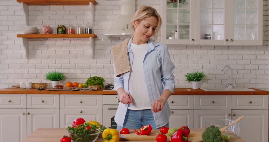 Portrait of happy smiling young woman preparing fresh healthy vegan salad with many vegetables standing in the kitchen at home. Vegetarian food, diet and nutrition concept. 4k video