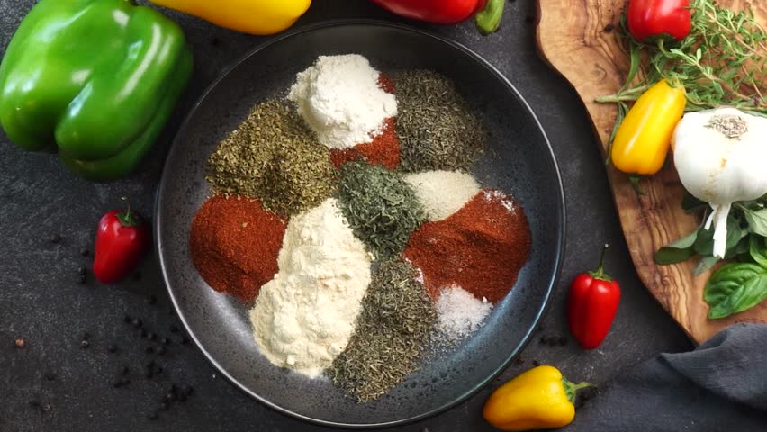 Making a vibrant Cajun Spice Blend, mixing red paprika, cayenne pepper, oregano, thyme, white garlic onion powder and black pepper in a bowl, creating a striking contrast against a black background.