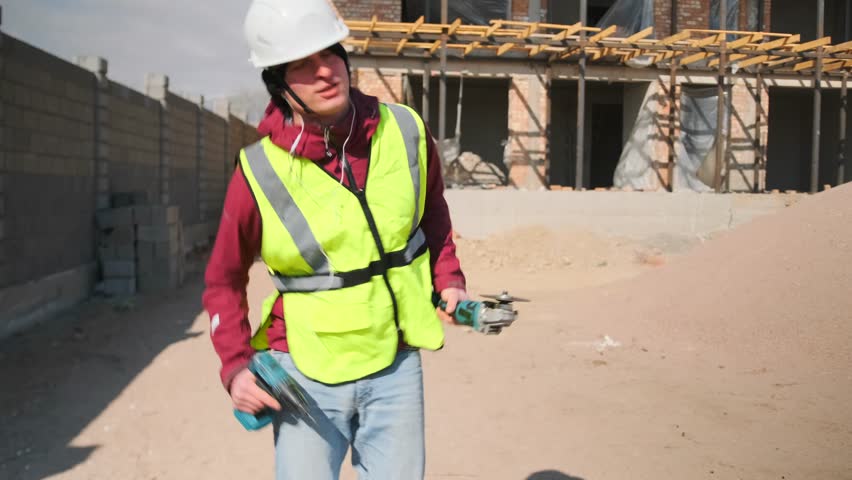 Immersed in music, a young construction worker in a hard hat and vest breaks into an uninhibited dance, grooving with a drill and saw. His movements radiate energy, drive, and playful joy.