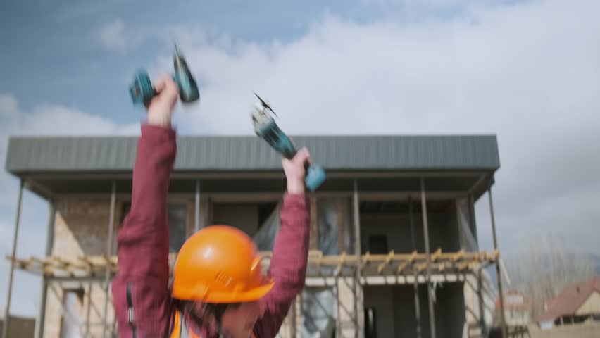 A cheerful construction worker in a hard hat and vest listens to music through earbuds, raising his hands and singing along. His upbeat moves bring rhythm and energy to the construction site.