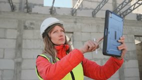 A female architect in a hard hat and vest stands on a construction site with a tablet and stylus, focused on reviewing blueprints and making adjustments to the building under construction. - Powered by Shutterstock - Get 15% off with code: PIKWIZARD15