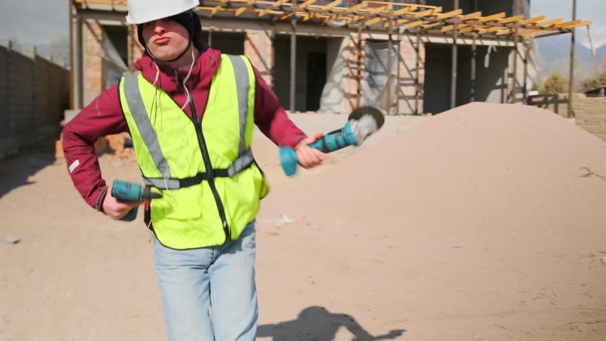 At a construction site, a young worker in a hard hat and vest dances with a saw and drill, his uninhibited, dynamic moves turning a quick break into a burst of raw energy and joy.