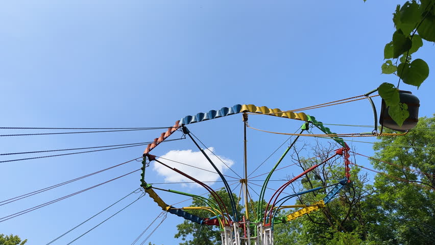 Low-angle view of a kids flying high on a colorful chain swing carousel ride against a blue sky.Carefree summer fun: A riders on a wave swinger attraction soars through the air at an amusement park
