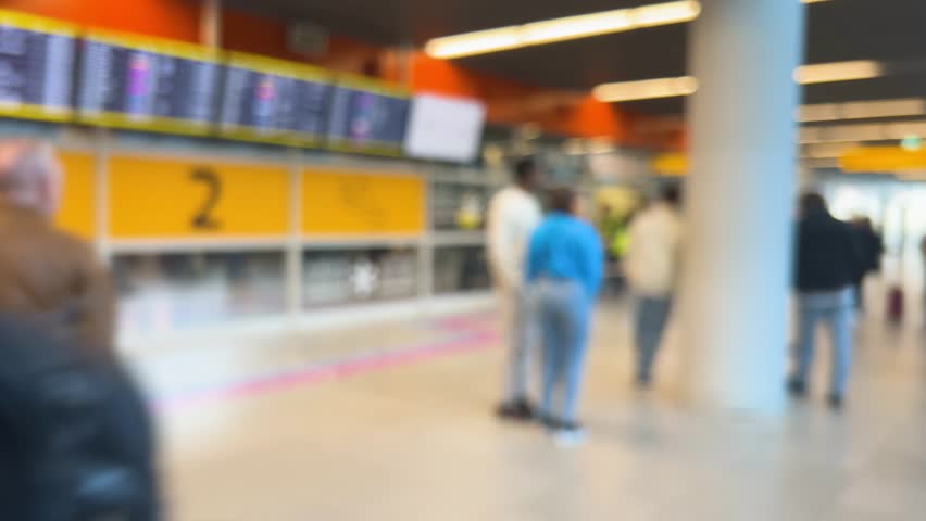 People waiting to greet passengers stand at arrival gate 2 at Warsaw Chopin Airport (WAW), Poland. Passengers arriving by plane exit with their luggage through automatic door. Out of focus.