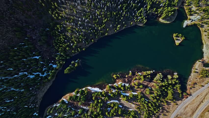 Curved lake bends through Frisco Gulch’s lush green pines in late afternoon light, top shot drone descend
