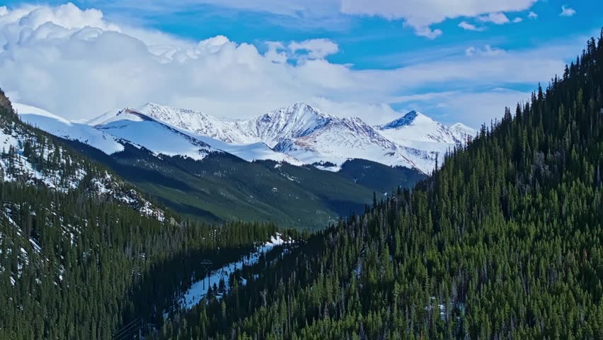 Drone tracking left reveal of forested hill with rocky cliffs and snow traces in Frisco Gulch