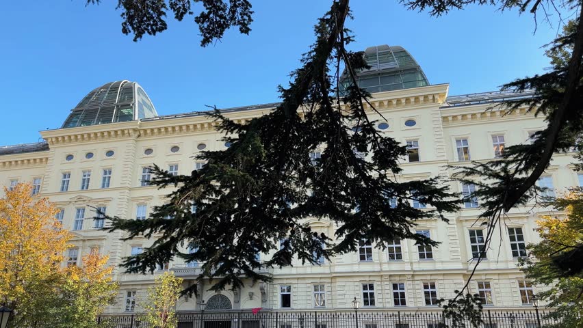 Historical building and palmhouse, as a part of the Hofburg Palace next the Burggarten, or City garden, Vienna, Austria. View through the branches while panning in autumn day
