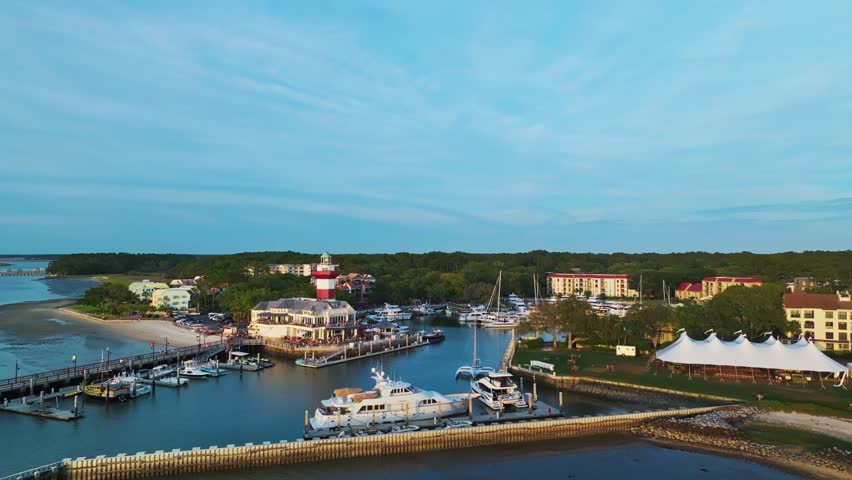 Harbor lighthouse with tourists visible on viewing deck during sunny day, angled approach over yacht, Harbour Town Pier South Carolina USA