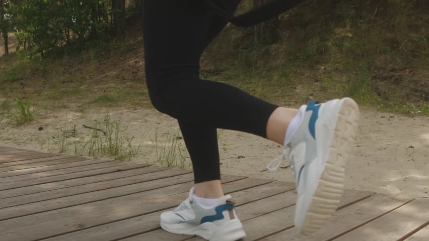 Woman legs running along wooden path in park, wearing black leggings and white sneakers during fitness training session, showcasing active lifestyle and outdoor exercise