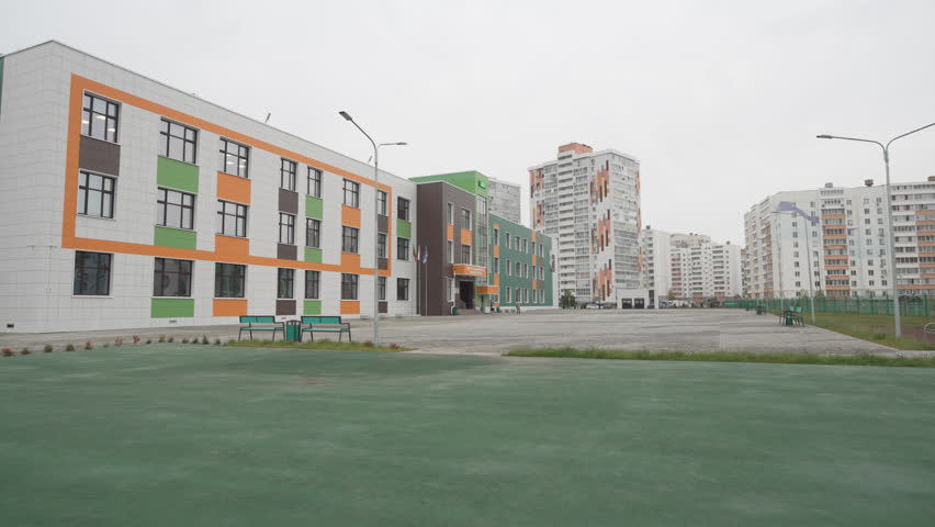 Multicolored school nestled between tall homes features cozy landscaped yard with benches. Space blends comfort and community spirit