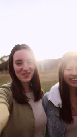 Four cheerful female friends are enjoying a sunny day at the park, laughing and embracing each other, creating a heartwarming scene of friendship and joy
