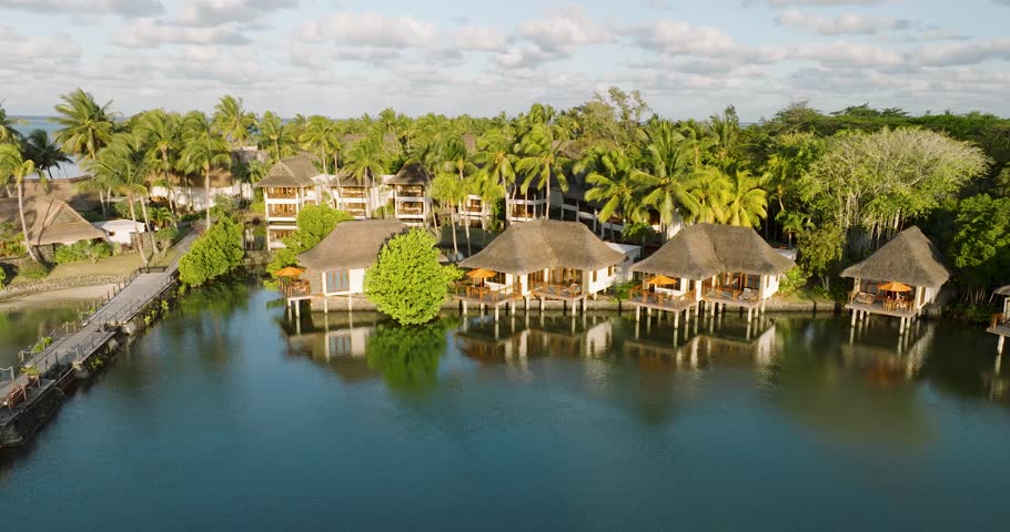Aerial view of luxurious bungalows and serene lagoon surrounded by palm trees and thatched roofs, Prince Maurice, Flacq, Mauritius.