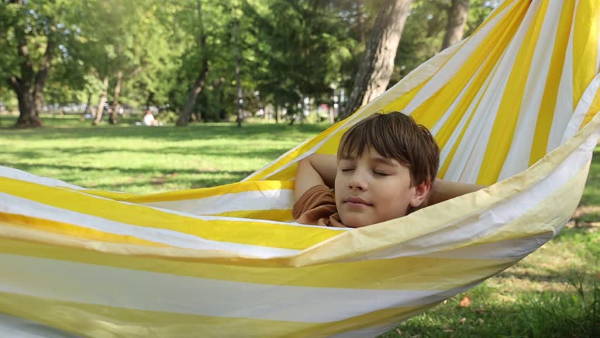 A portrait laughing preteen boy lies in a hammock having fun summer outdoor. Generation Z. Happy childhood.
