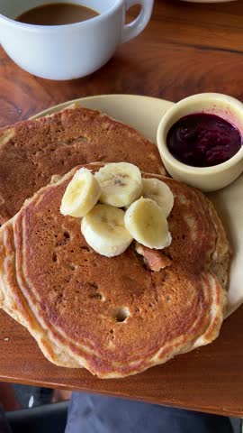 Maple syrup is poured on pancake with banana for breakfast in cafe or restaurant. Fancy bistro shop with delicious menu filmed from phone pov of foodie person or influencer eating out in city downtown
