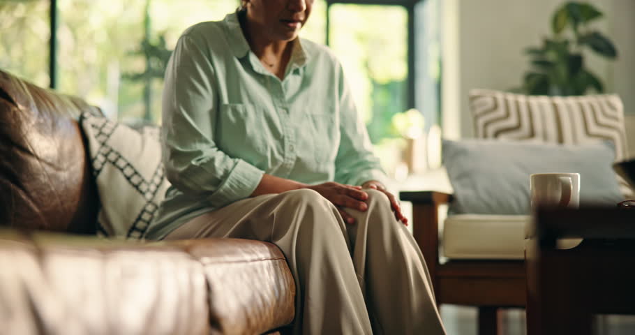 Home, legs and senior woman with pain, stretching or pensioner with arthritis, inflammation or hurt. Sore, knees and elderly person with osteoporosis, injury and massage for joint, tension and house