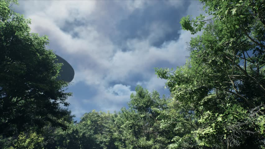 Breathtaking view up through the canopy in a forest as a huge circular UFO flying saucer spins slowly overhead casting its ominous shadow over the trees below