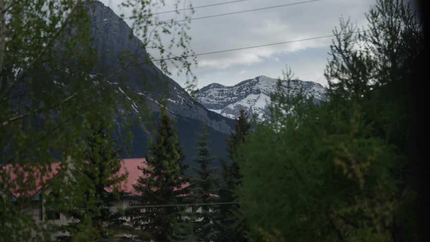 Panoramic view of valley and forested hills with mountain backdrop under cloudy morning sky, reveal behind chain out of focus