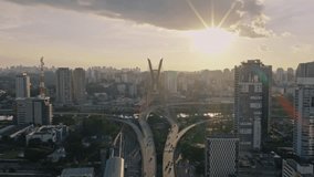 Drone zooms in on Octavio Frias de Oliveira bridge during golden hour with the sun setting behind the city skyline. - Powered by Shutterstock - Get 15% off with code: PIKWIZARD15