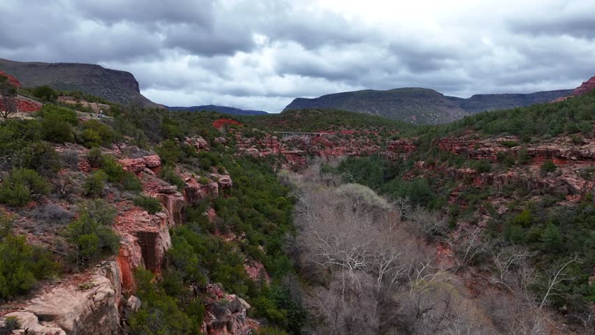 Aerial view of the majestic Midgley Bridge over a scenic canyon and valley with red rocks and greenery, Oak Creek, Arizona, United States.
