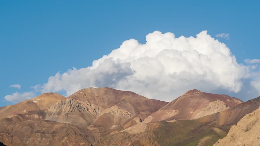 A Static time-lapse footage of sunset to past blue hour near Maipo Volcano. Clouds move and dissipate over rugged mountains under a blue sky