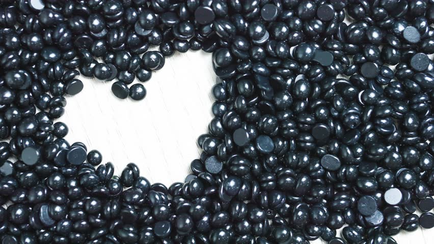 Glossy black hard wax beans forming heart shape against rustic white wooden surface, highlighting skincare aesthetic with minimalist composition