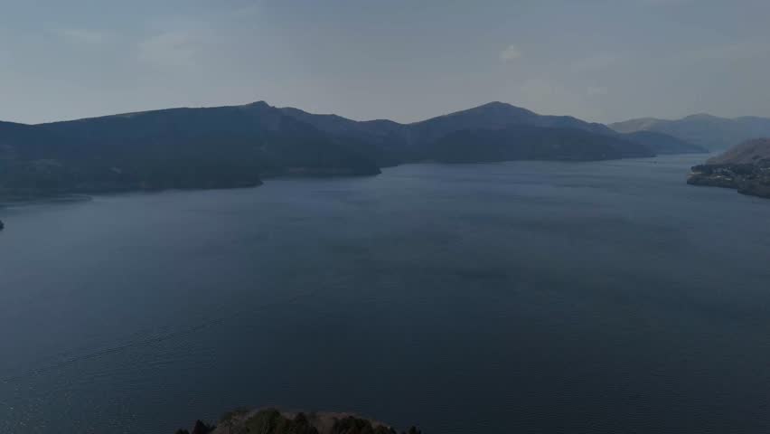 A Tranquil view of Lake Ashi, Japan, surrounded by misty mountains under a calm blue sky