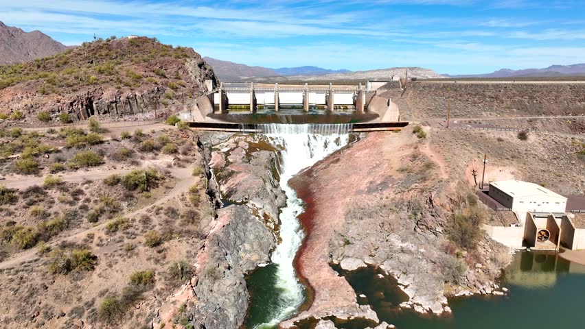 Aerial view of a majestic dam and waterfall cascading into a tranquil river surrounded by rocky mountains, Black Canyon City, Arizona, United States.