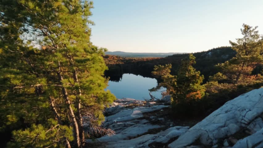 A lake surrounded by vegetations and rugged quartzite cliffs at the golden hour in the serene backcountry of Killarney Provincial Park in Ontario