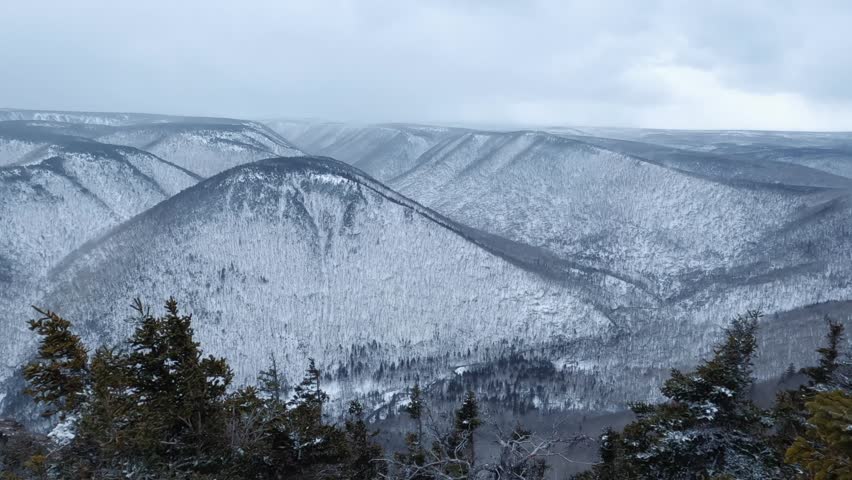 A view from the top of the Sugar Loaf hike in Cape Breton, Nova Scotia during winter. The foggy sky sets dramatic tone as snow covers the mountains