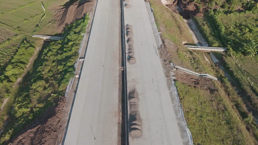 Aerial View of Construction Progress on a Rural Road Surrounded by Lush Greenery and Natural Landscapes