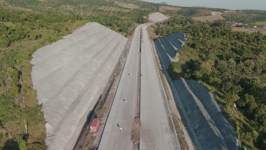 Aerial View of New Road Construction Surrounded by Lush Hills and Clear Blue Skies