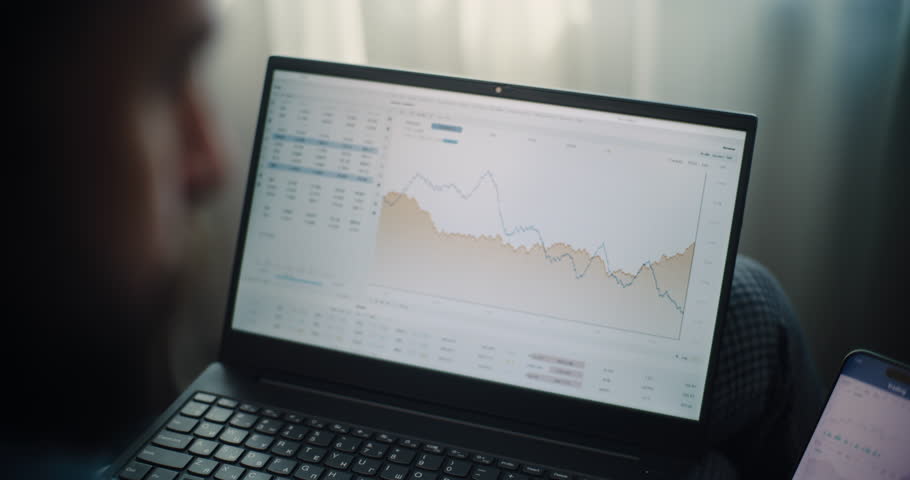Close Up of Stock Exchange Broker Using Laptop and Smartphone, Monitoring Real-Time Stocks and Exchange Market Charts in Online Trading Software. Successful Investment Agent Working in Home Office.