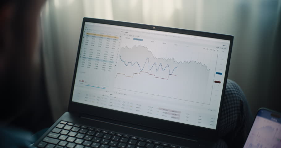 Close Up of Stock Exchange Broker Using Laptop and Smartphone, Monitoring Real-Time Stocks and Exchange Market Charts in Online Trading Software. Successful Investment Agent Working in Home Office.