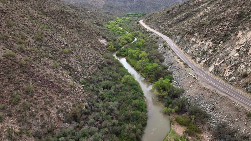 Aerial view of the serene Gila River winding through a picturesque valley surrounded by rugged mountains and lush greenery, Pinal County, Arizona, United States.