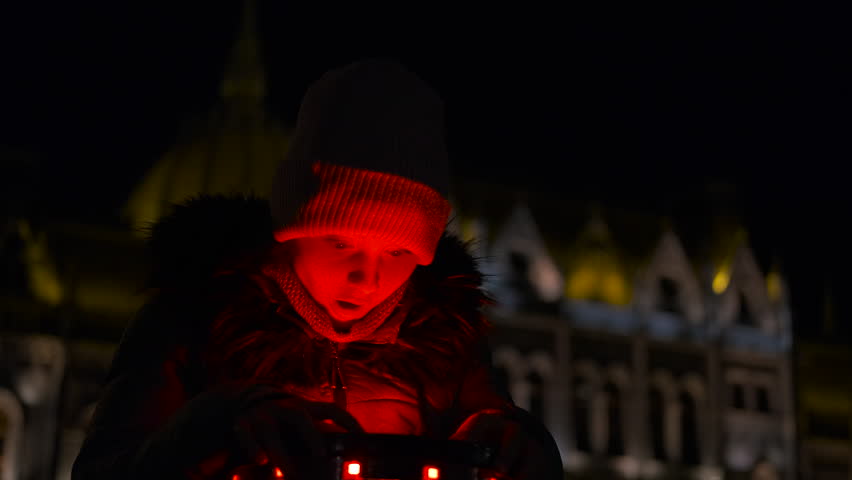 Child playing with a red-lit toy at night in front of hungarian parliament building. Enthusiastic child plays with a red glowing toy in front of the illuminated hungarian parliament building at night