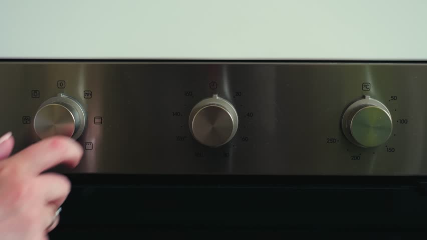 Temperature control knob on sleek stainless steel stove, adjusting heat for precise cooking in modern kitchen environment.