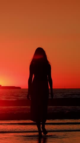 Attractive Asian woman enjoys a walk on the beach at sunset in Southern California. Slow Motion. Vertical Video.