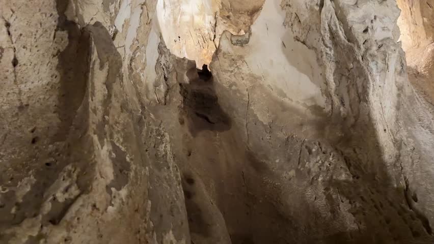 A dramatic view of ocean waves crashing into a volcanic sea cave, with rugged rock formations and sunlight illuminating the cave interior.