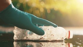 Hand in blue glove picking up plastic bottle from puddle with water drops falling slow motion environmental cleanup - Powered by Shutterstock - Get 15% off with code: PIKWIZARD15