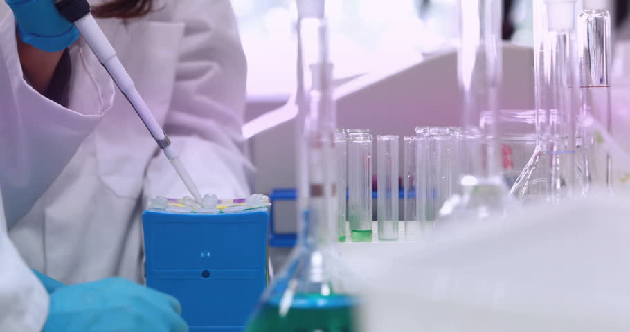 Female scientist picking up micropipette at lab bench, aspirating sample and dispensing into rack. Laboratory, research, science, precision, instrumentation, purity, experimentation