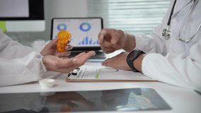 Two doctors are sitting at a desk with a bottle of pills and a laptop. One of the doctors is pointing at the pills - Powered by Shutterstock - Get 15% off with code: PIKWIZARD15