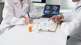 Two doctors are sitting at a table with a laptop and a clipboard. One of them is pointing at a graph on the laptop - Powered by Shutterstock - Get 15% off with code: PIKWIZARD15